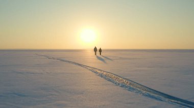 The two tourists going through the snow field against beautiful sky