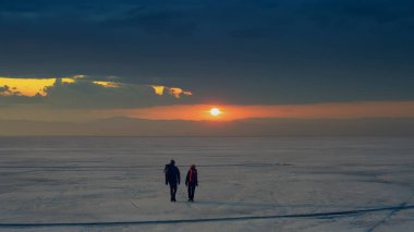 The two people with backpacks going through the snow field against beautiful sky