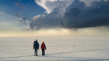 The two people with backpacks going through the snow field against beautiful sky