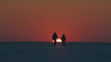 The two tourists going through the snow field against beautiful sunset
