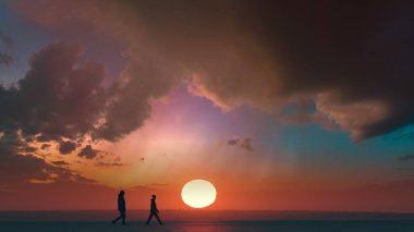 The couple of travelers walking through the snow field on sunset background
