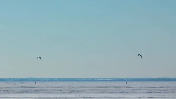 The two people doing snowkiting on the icy snow field