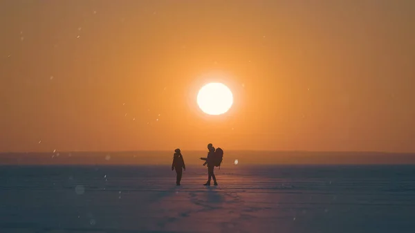 Two Travelers Walking Snow Field Sunset Background – stockfoto
