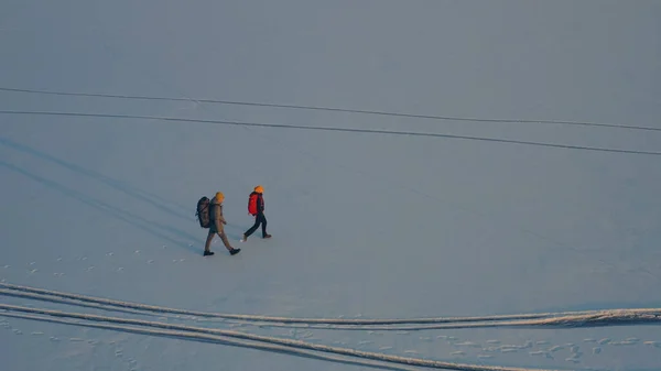 The upper view on two tourists trekking through the icy field