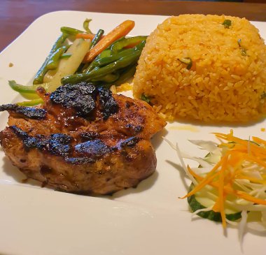 Tavuklu biftek ve sotelenmiş sebzeli kızarmış pilav tabakta servis edilir. Tavuk biftek tabağı.