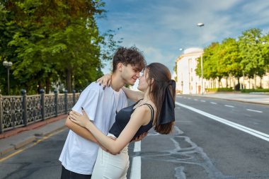 Genç bir adam ve bir kız yazın şehirde yolda sarılıyorlar..