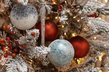 Noel oyuncakları karla kaplı bir Noel ağacında asılı duruyor.