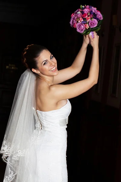 Sorrindo noiva no vestido de casamento branco está jogando fora seu buquê de casamento . — Fotografia de Stock