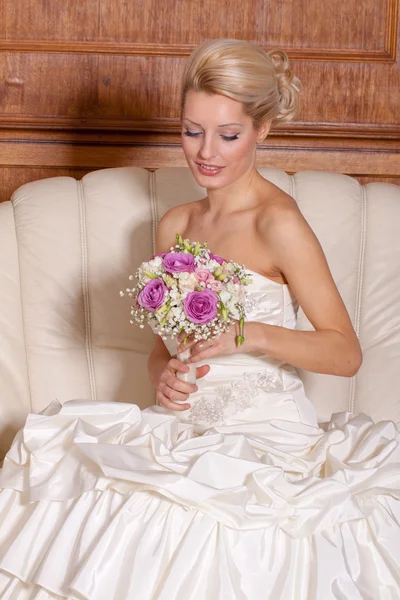 Indoor portrait of adorale bride with blond hair sitting on a sofa. — Stock Photo, Image