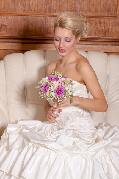 Indoor portret van adorale bruid met blond haar zittend op een bank. — Stockfoto