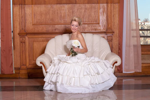 Indoor portret van mooie bruid met blonde haren zittend op een bank. — Stockfoto
