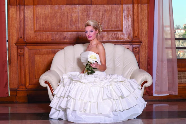 Retrato interno de noiva bonita com cabelo loiro sentado em um sofá . — Fotografia de Stock