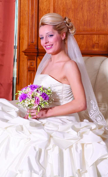 Indoor portrait of sexy bride with blonde hair sitting on a sofa. — Stock Photo, Image