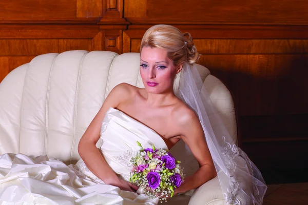 Indoor close up portrait of charming bride with blonde hair sitting on a sofa. — Stock Photo, Image