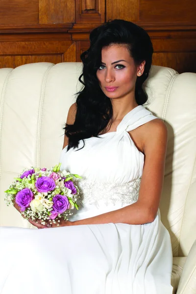 Indoor portrait of beautiful bride with black long hair sitting on a sofa. — Stock Photo, Image