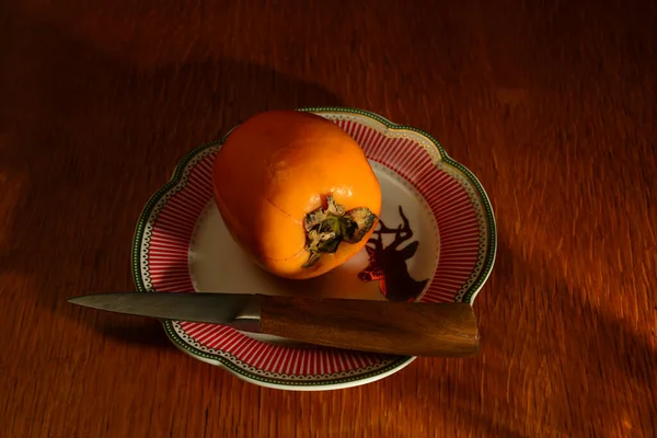 Caqui maduro y un cuchillo en un plato sobre la mesa — Foto de Stock
