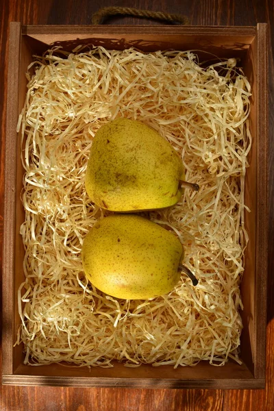 Two ripe pears in a box with shavings on a wooden table, close-up, top view — Stock Fotó