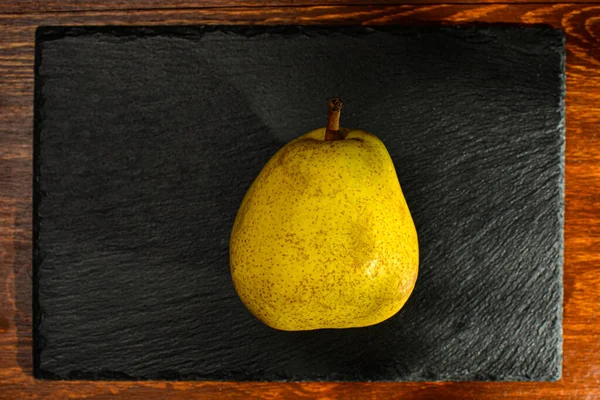 Natural yellow pear on a slate board, close-up, on a wooden table, top view — Stockfoto