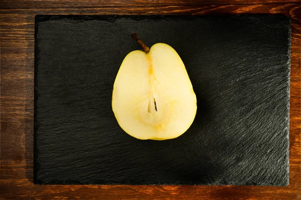Half natural yellow pear on a slate board, close-up, on a wooden table, top view — ストック写真