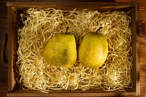 Two ripe pears in a box with shavings on a wooden table, close-up, top view — Stock Fotó