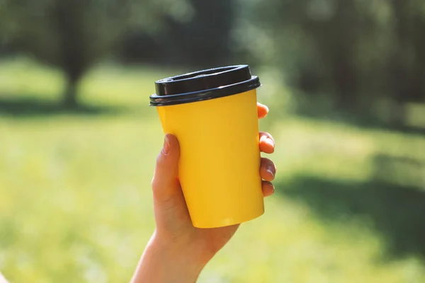 Geel Papieren Koffiekopje Mensenhand Een Zonnige Dag Een Groene Wazige Stockfoto