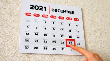 2021 duvar takviminin güzel bir Aralık sayfasındaki yakın plan ve bir erkek el kırmızı imleci Noel tarihine taşıyor