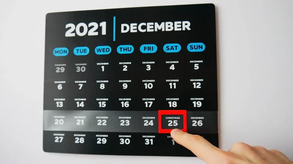 2021 duvar takviminin siyah ve güzel bir Aralık sayfasındaki yakın çekim ve bir erkek el kırmızı imleci Noel tarihine taşıyor