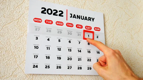 2022 duvar takviminin ilk sayfasını kapat ve bir erkek el kırmızı imleci 1 Ocak tarihine taşı