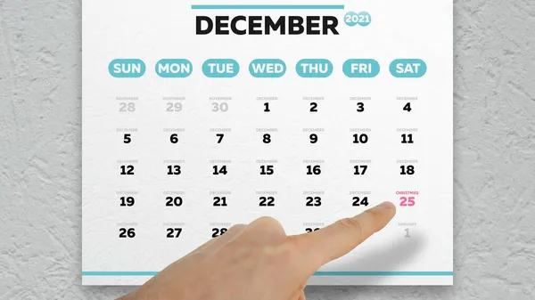2021 yılının Aralık sayfasındaki Noel tarihine işaret eden bir erkeğin yakın plan fotoğrafı.