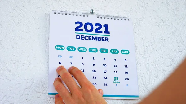 Bir adamın elinin Aralık sayfasındaki 2021 duvar takviminde üzerinde yılbaşı tarihi yazan yakın plan fotoğrafı.