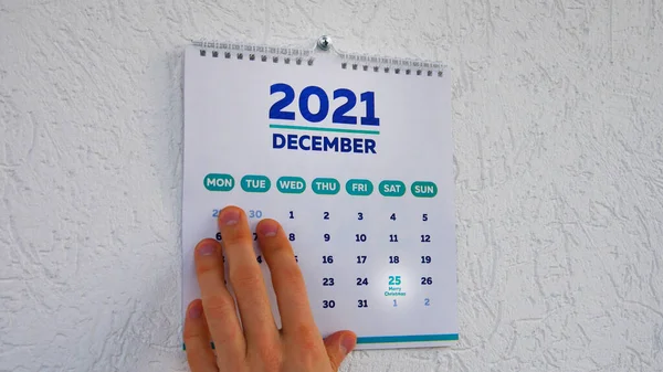 2021 yılının Aralık sayfasındaki Noel tarihi ve yanında bir erkek eli olan duvar takviminin yakın çekimi.