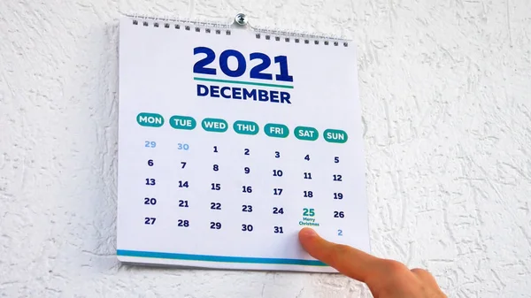 2021 duvar takviminin Aralık sayfasıyla Noel tarihini gösteren bir adam.