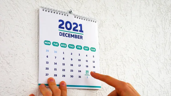 2021 yılı duvar takviminin Aralık sayfasıyla Noel tarihini gösteren bir adamın elleri.