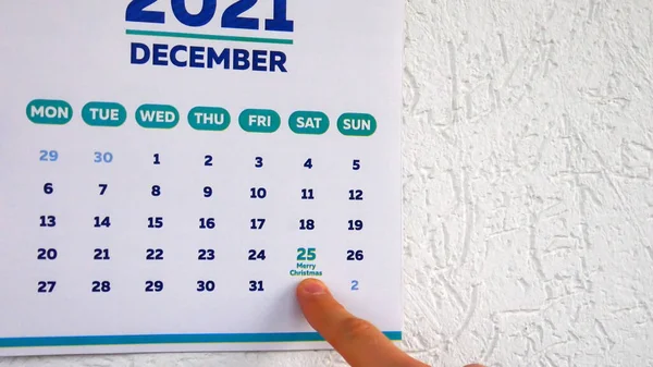 Bir duvar takvimi 2021 'in Aralık sayfasındaki yakın plan ve üzerinde Noel tarihini gösteren bir erkek eli.