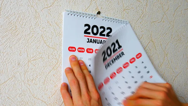 Duvarda 2021 takviminin Aralık sayfasındaki yırtılan bir adamın ellerini yakın plan 2022 yılının Ocak sayfasındaki yeni takvim takip ediyor.