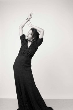 Stüdyoda sağlam bir arkaplan önünde şık siyah elbiseli güzel bir kadın manken.