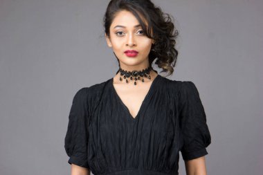 Stüdyoda sağlam bir arkaplan önünde şık siyah elbiseli güzel bir kadın manken.