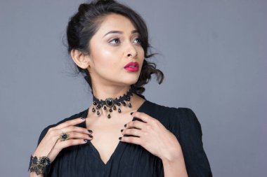 Stüdyoda sağlam bir arkaplan önünde şık siyah elbiseli güzel bir kadın manken.