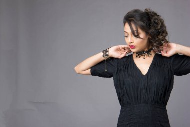 Stüdyoda sağlam bir arkaplan önünde şık siyah elbiseli güzel bir kadın manken.