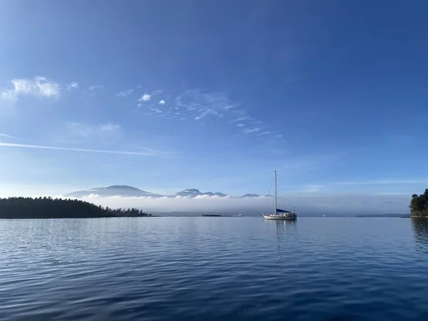 A single sailboat at anchor with calm water and blue skies — Stock Photo, Image