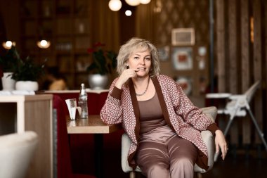 Bir kafede zarif bir takım elbise giymiş yetişkin, güzel sarışın bir kadının portresi.