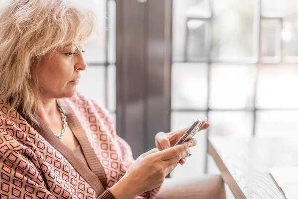 Telefone Celular Nas Mãos Uma Mulher Loira Adulta Atraente Sentada Imagens De Bancos De Imagens Sem Royalties