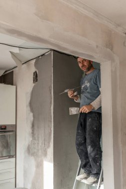 Avrupalı görünümlü bir adam duvarları kaplıyor, daireyi onarıyor, evi onarıp yeniden dekore ediyor.