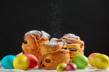 Paskalya pastaları, geleneksel renkli yumurtalar şenlik masasında, koyu arkaplanda.