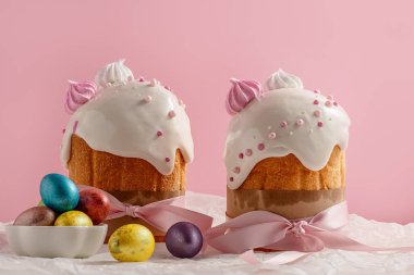 Paskalya pastaları, geleneksel renkli yumurtalar şenlik masasında, pembe arka planda.