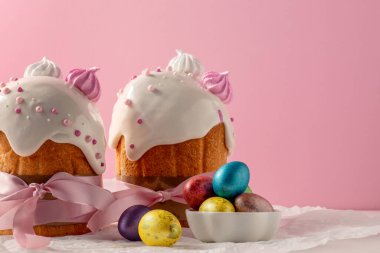 Paskalya pastaları, geleneksel renkli yumurtalar şenlik masasında, pembe arka planda.