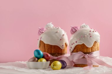 Paskalya pastaları, geleneksel renkli yumurtalar şenlik masasında, pembe arka planda.
