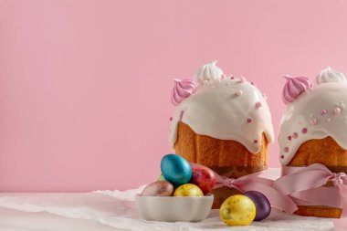 Paskalya pastaları, geleneksel renkli yumurtalar şenlik masasında, pembe arka planda.