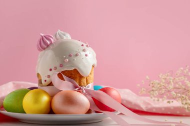 Paskalya pastaları, geleneksel renkli yumurtalar şenlik masasında, pembe arka planda.