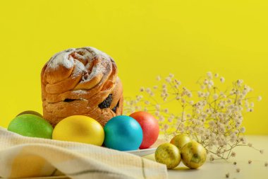 Paskalya pastaları, geleneksel renkli yumurtalar şenlik masasında, sarı arka planda.